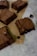 Several square pieces of rich, chocolate brownies are placed on a sheet of parchment paper. The brownies have a crispy top and a dense, moist texture. They are arranged on a marble surface with some crumbs scattered around.