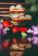Hand holding a stacked sandwich bursting with layers of fresh ingredients against a rustic wooden background.
