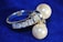 A silver ring adorned with two large pearls and several small rectangular crystals, set against a deep blue background. The pearls are prominently featured, contrasting with the shimmering metal and sparkling stones, giving the piece an elegant appearance.