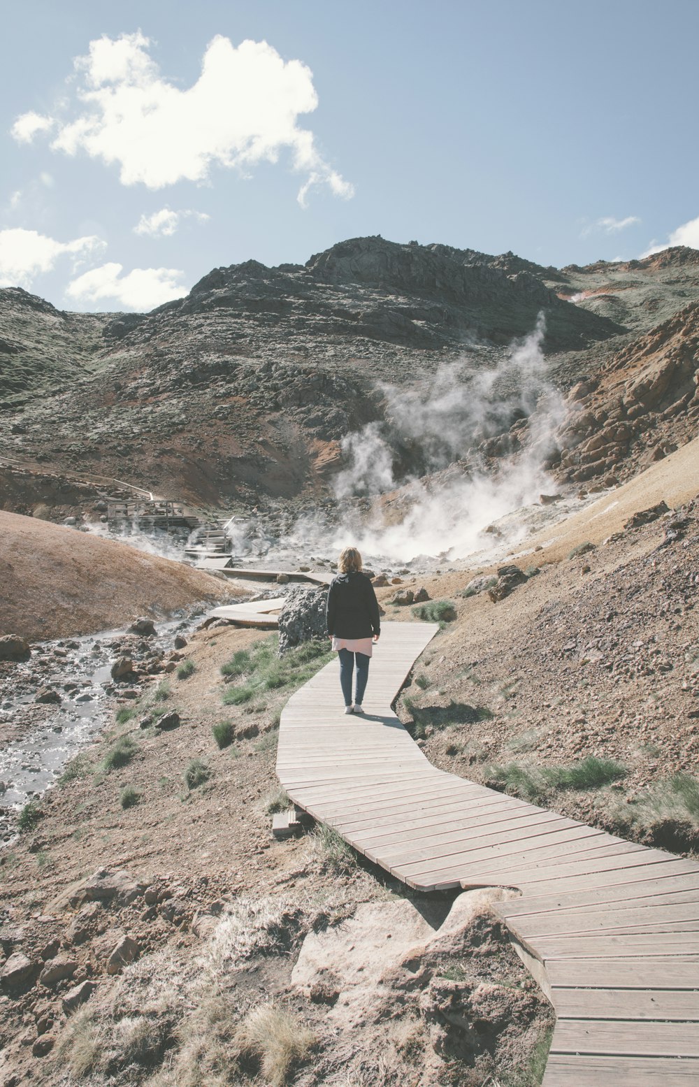 person in black jacket and blue denim jeans walking on brown wooden pathway during daytime