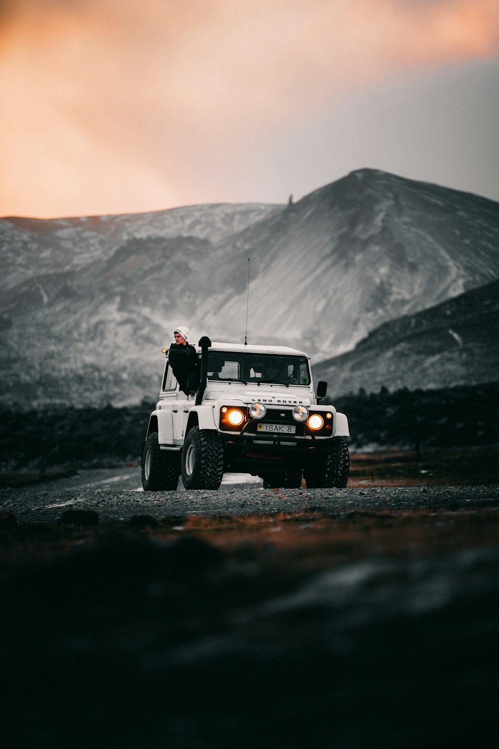Hombre con chaqueta y pantalones negros de pie junto a un jeep wrangler blanco en la carretera durante el día