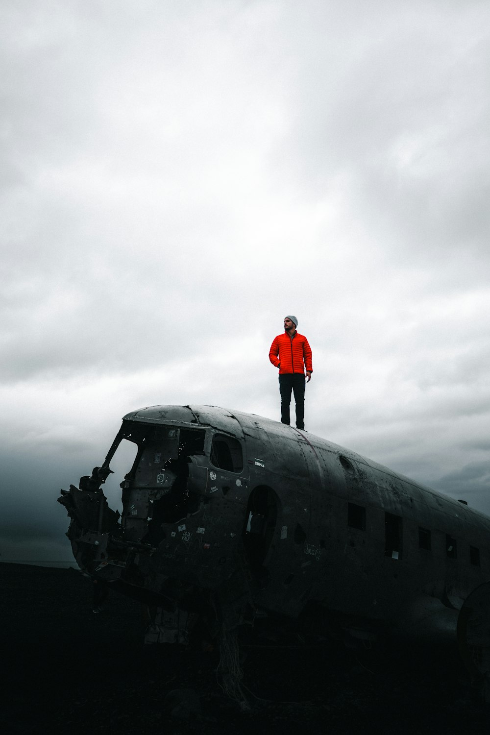 man in red jacket standing on black airplane under gray cloudy sky during daytime