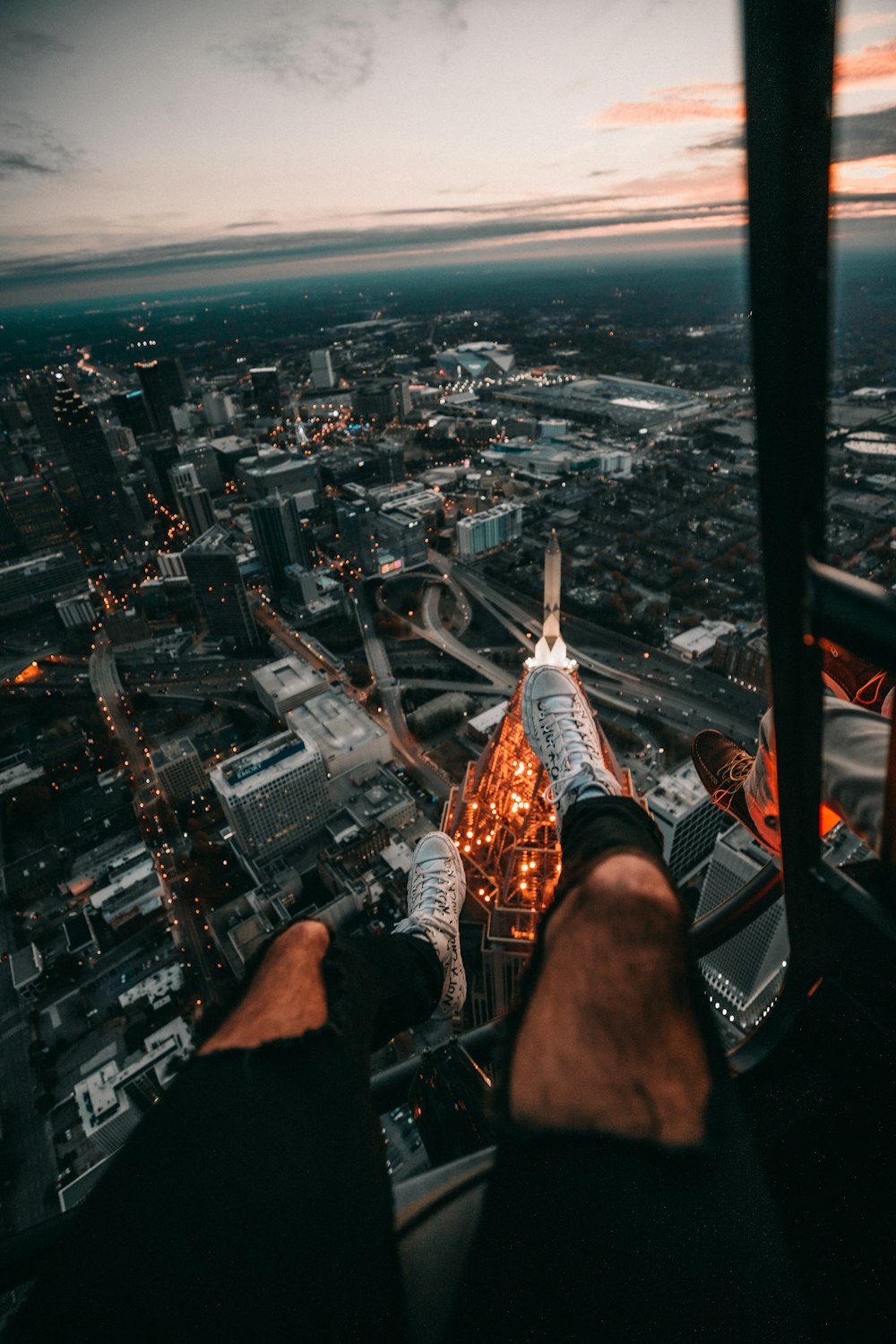 person in black pants and brown shoes sitting on top of building looking at city during