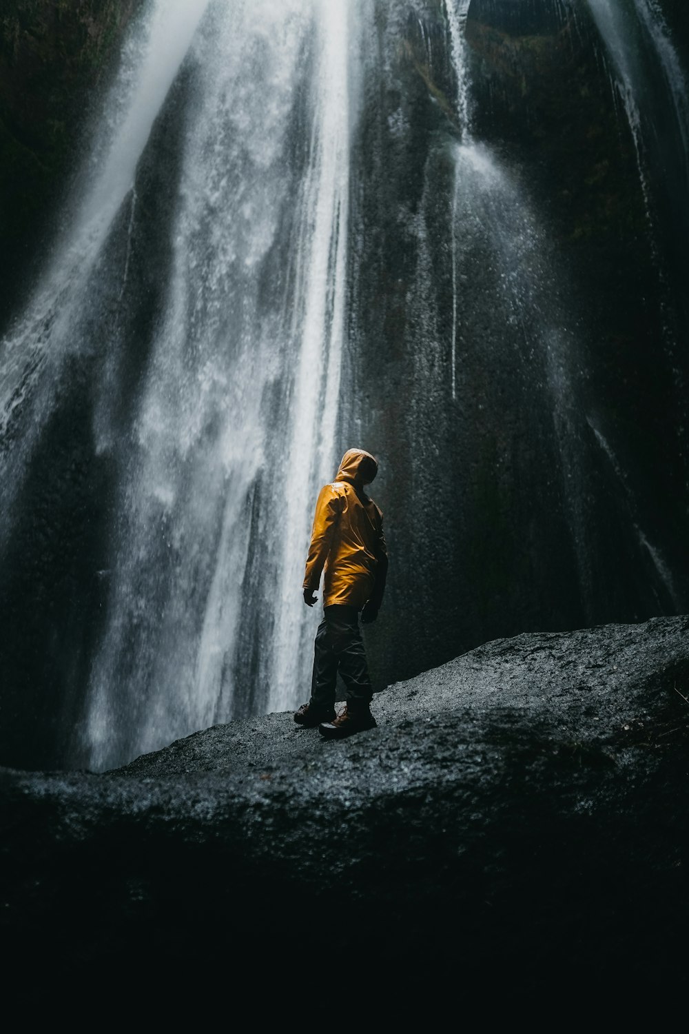 man in brown jacket standing in front of waterfalls