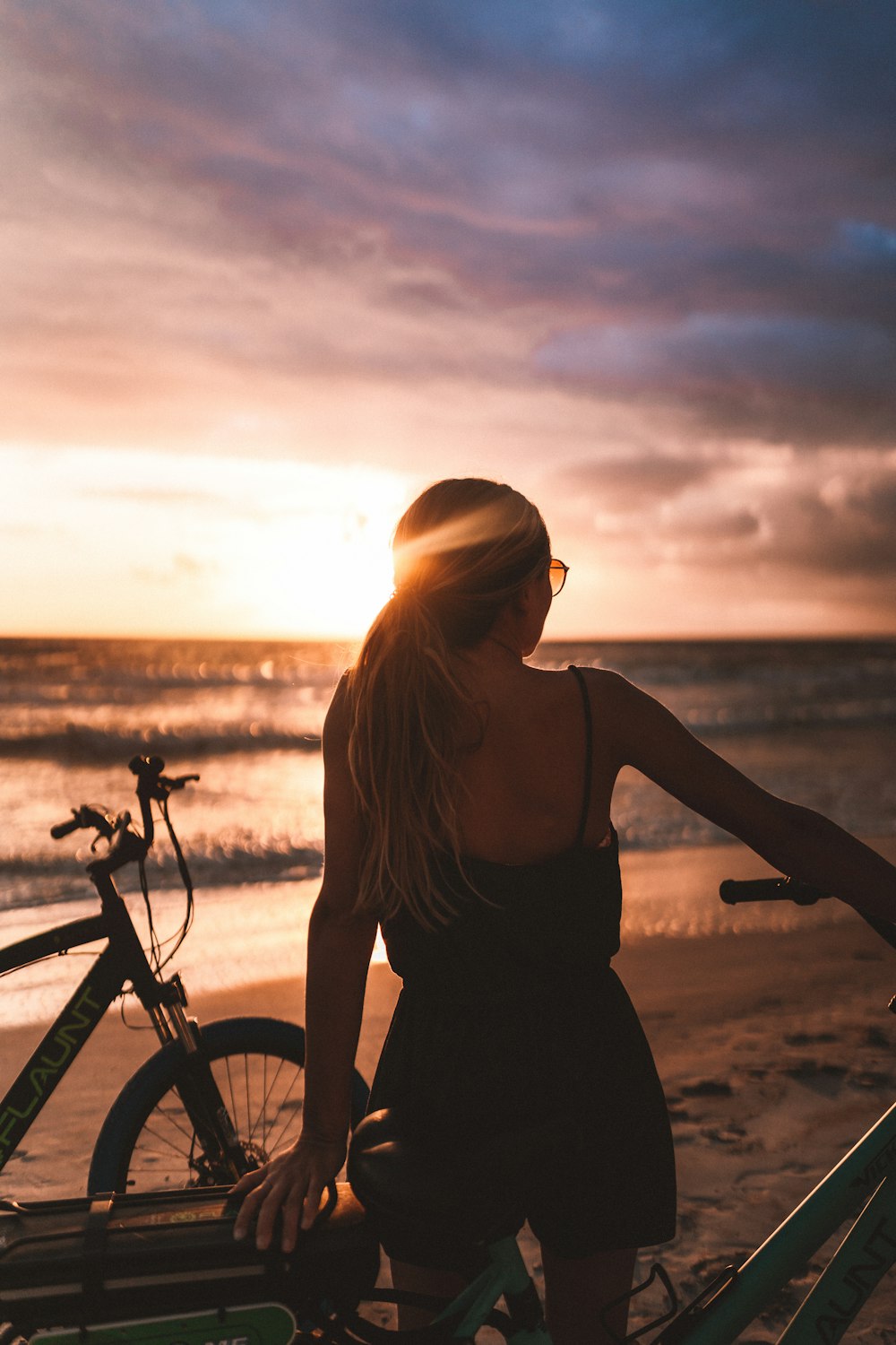 woman in black tank top and black skirt standing beside bicycle during sunset