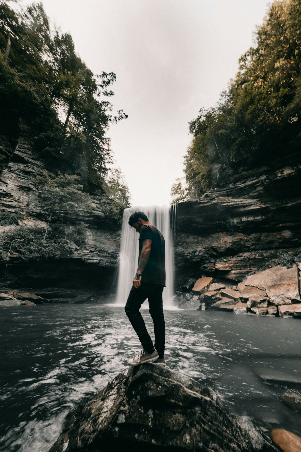 woman in white jacket and black pants standing on rock near waterfalls during daytime