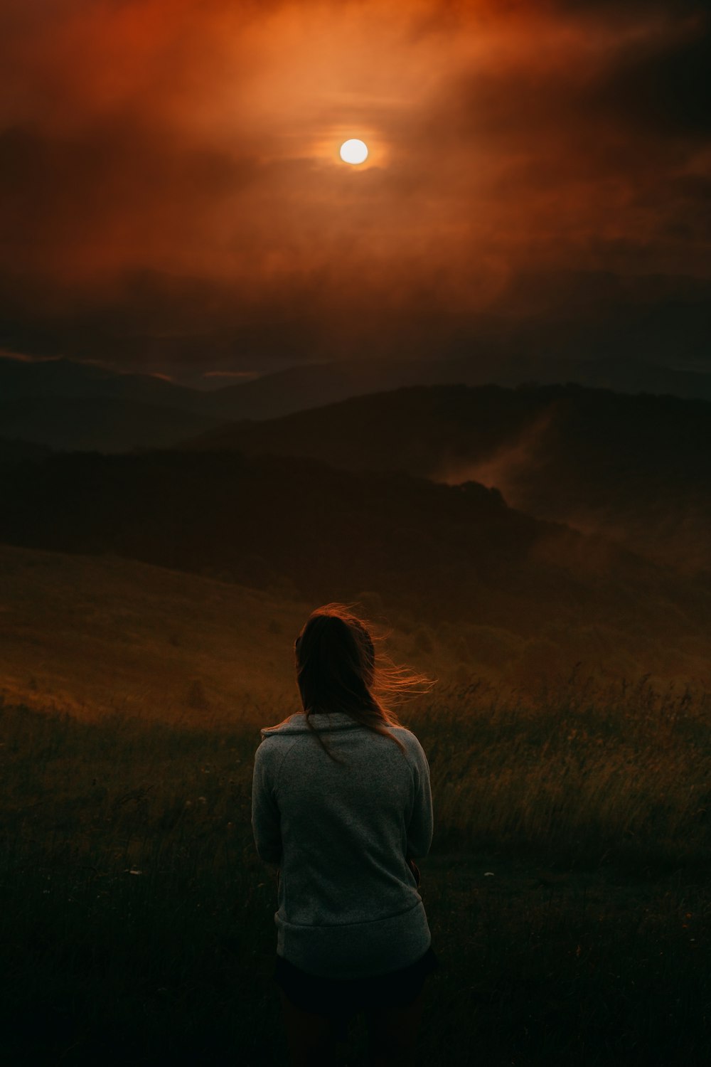 woman in gray long sleeve shirt standing on green grass field during sunset