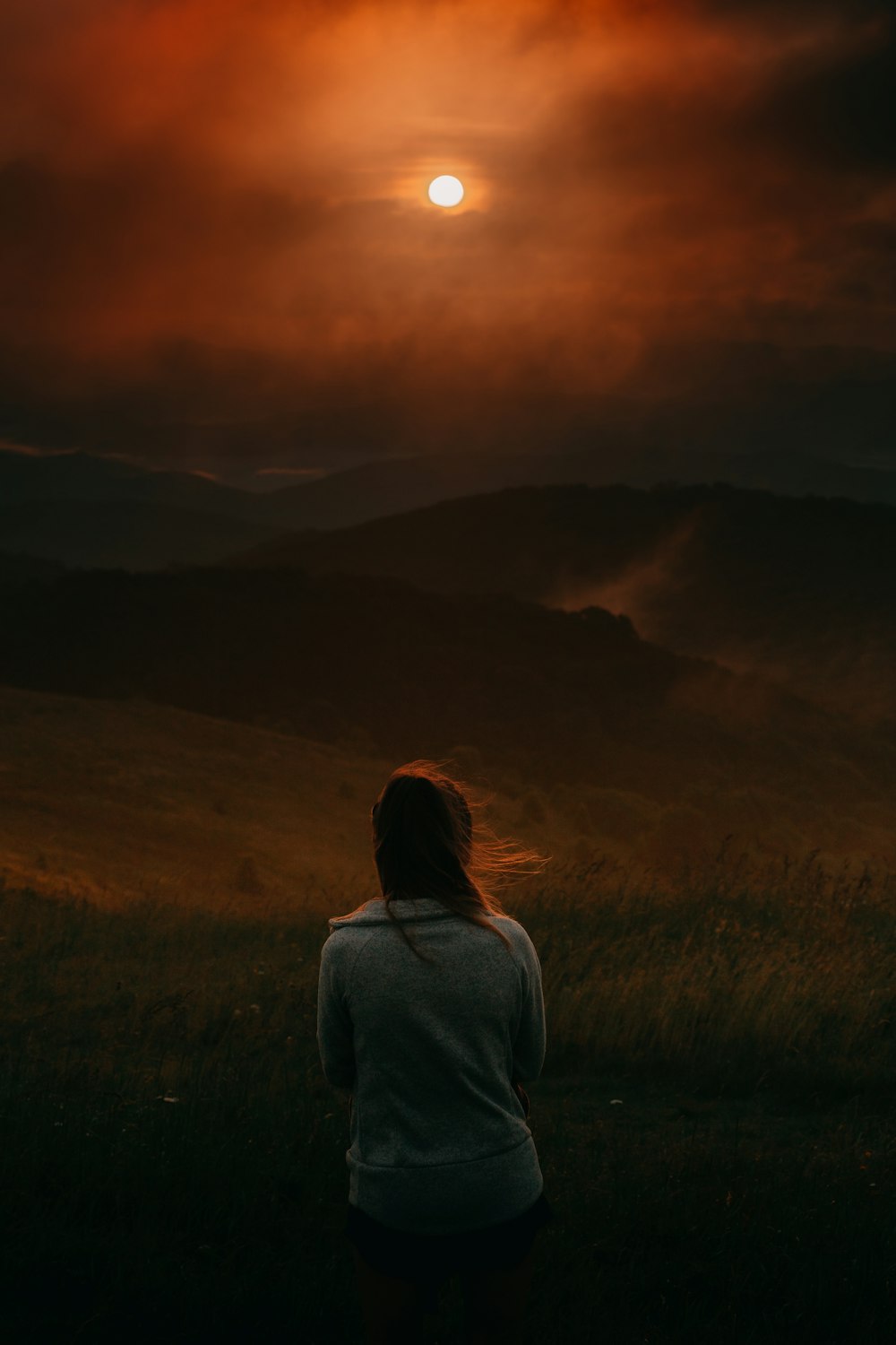 Mujer en camisa gris de manga larga de pie en el campo de hierba verde durante la puesta del sol
