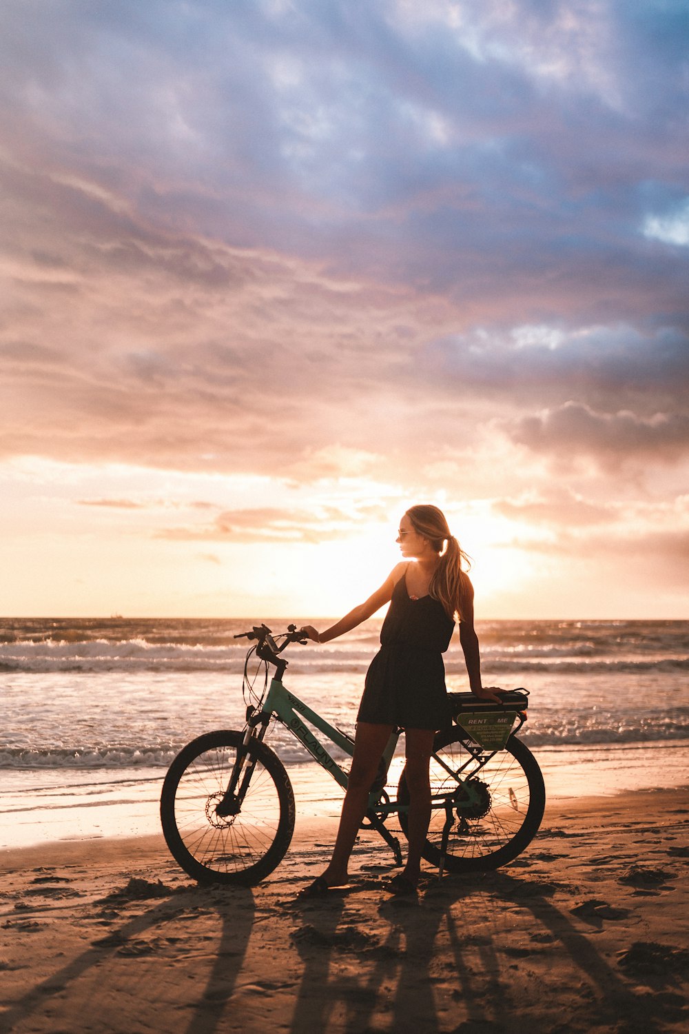 woman in black tank top riding on bicycle on beach during sunset