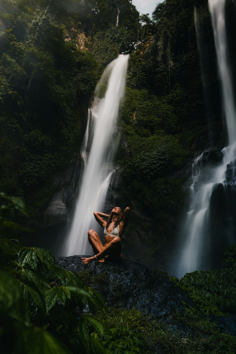 woman in brown dress sitting on rock near waterfalls during daytime