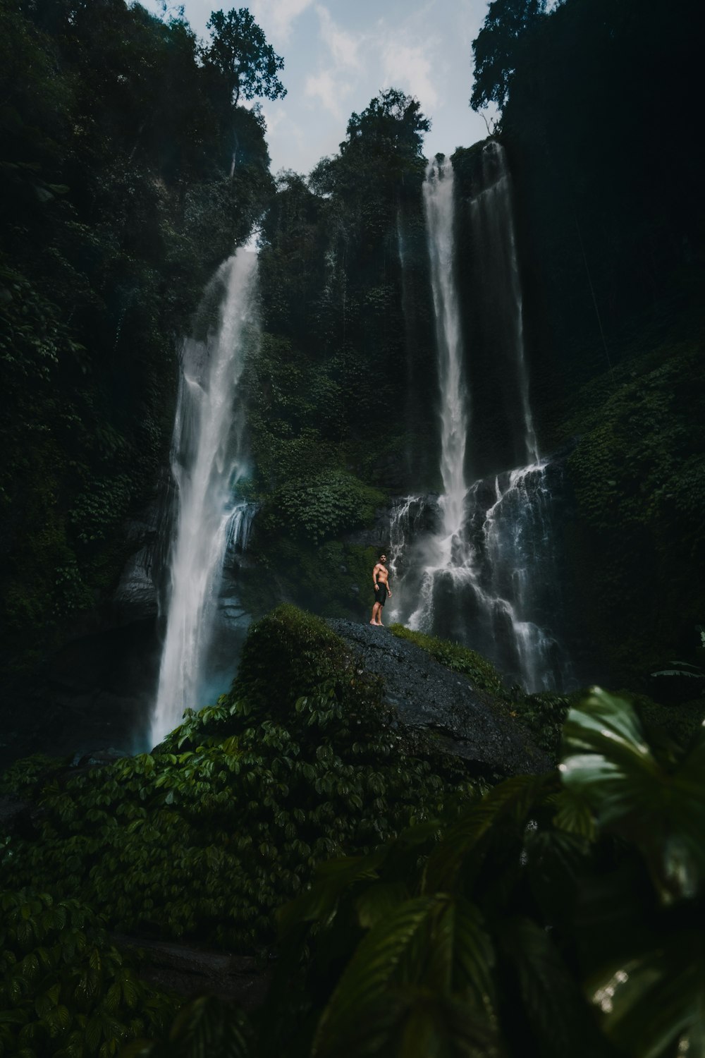 person in black jacket standing on rock near waterfalls during daytime