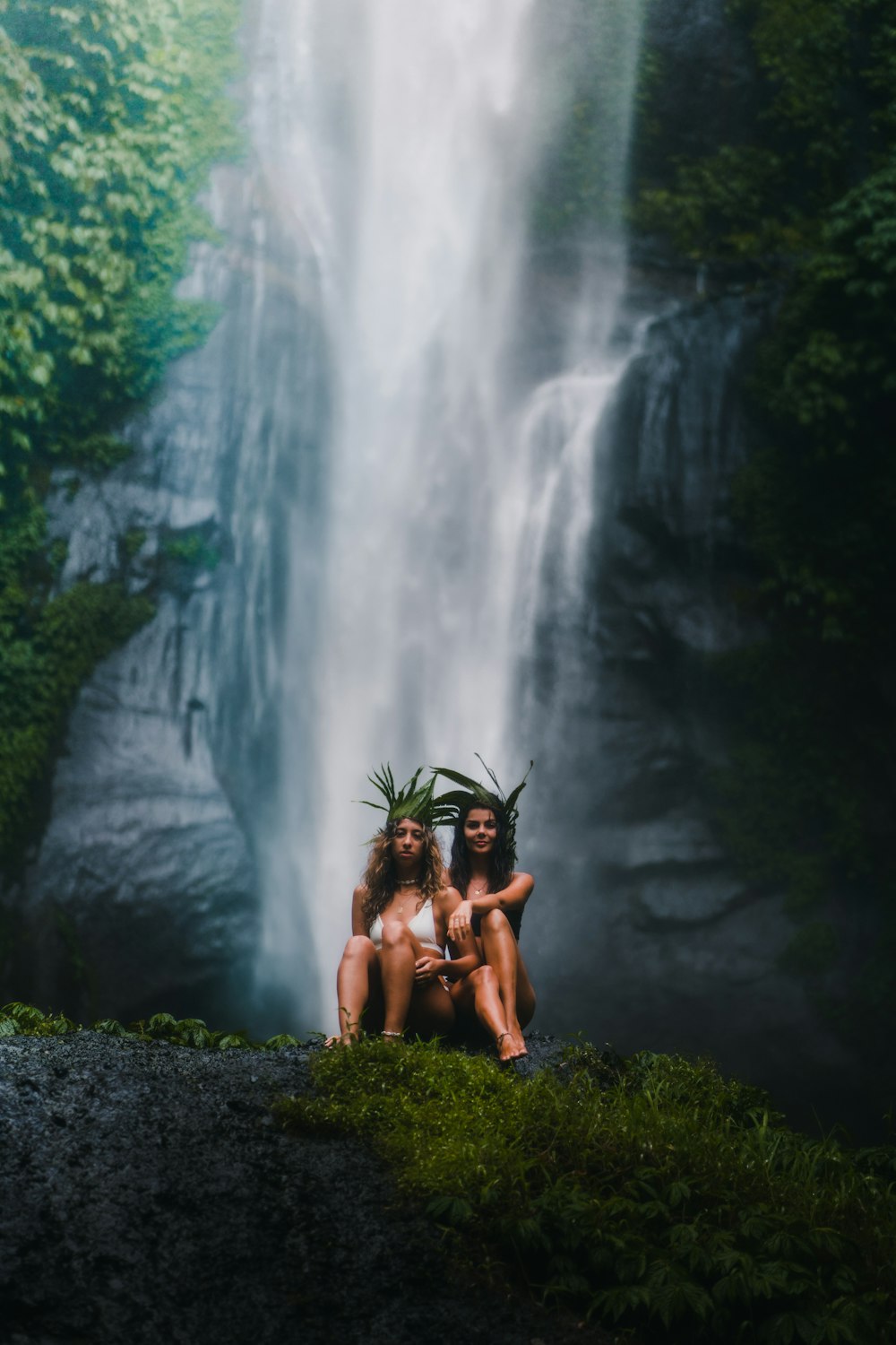 2 women sitting on rock near waterfalls during daytime
