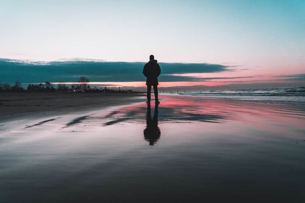 Silueta del hombre de pie en la orilla del mar durante la puesta del sol
