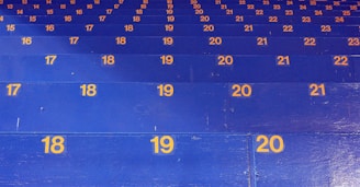 A series of blue stadium seats are arranged in rows, each marked with sequentially increasing yellow numbers. The numbers appear to organize the seating in an orderly fashion and climb in value from 15 to 24.
