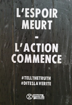 The image features a text in French that reads 'L'espoir meurt - L'action commence' which translates to 'Hope dies - Action begins.' Below this text are the hashtags '#TELLTHETRUTH' and '#DITESLAVERITE.' At the bottom, there is an Extinction Rebellion logo.