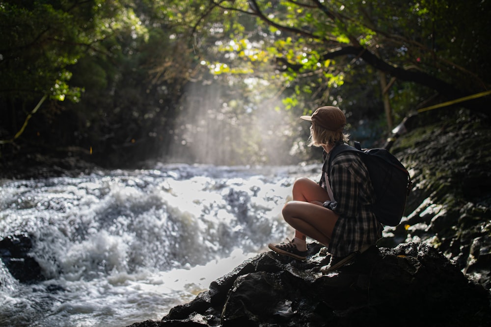 man in black and white plaid shirt sitting on rock near river during daytime