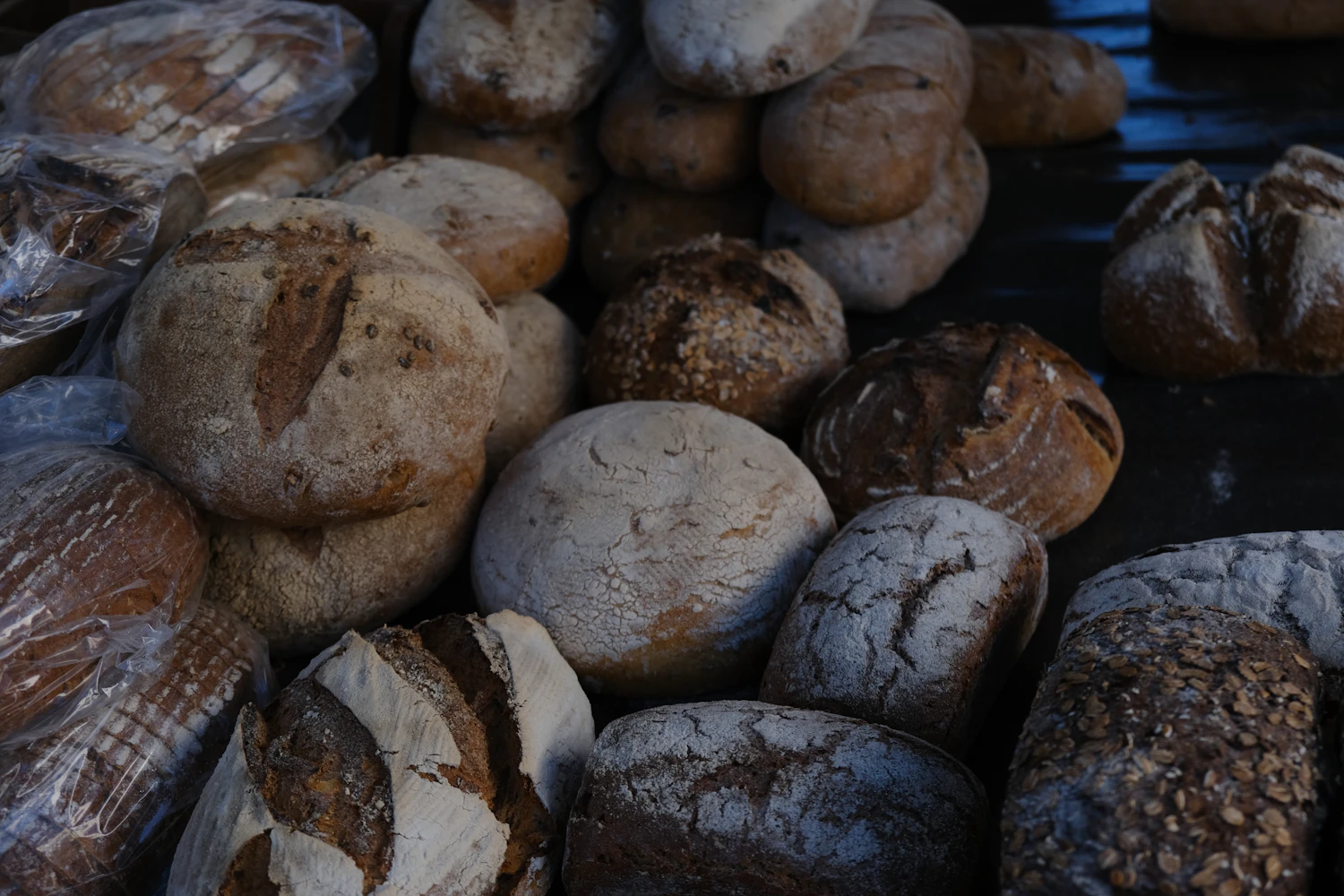 A heap of dark rustic loaves tipped together on a bench