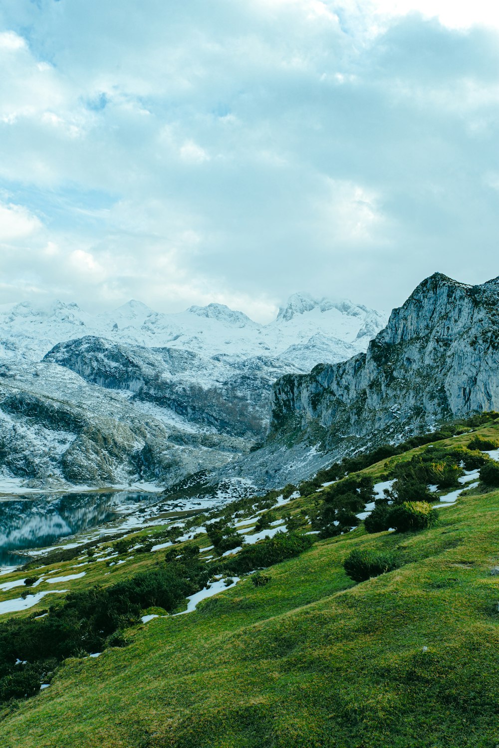 green grass field near snow covered mountain under white cloudy sky during daytime