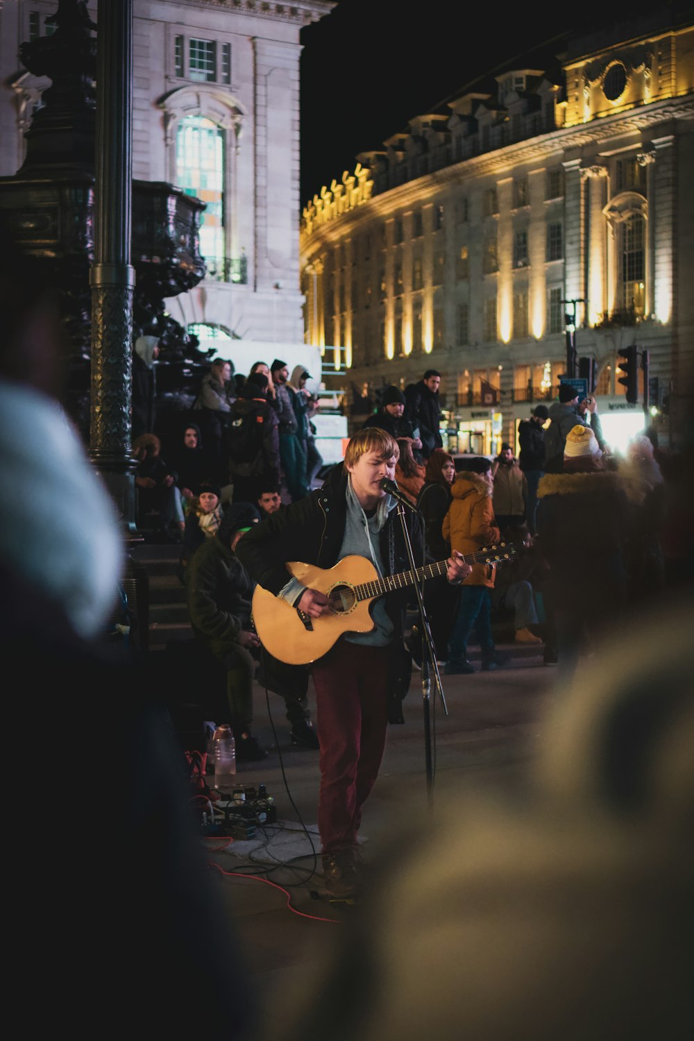 Hombre con camiseta negra tocando la guitarra en la calle durante la noche