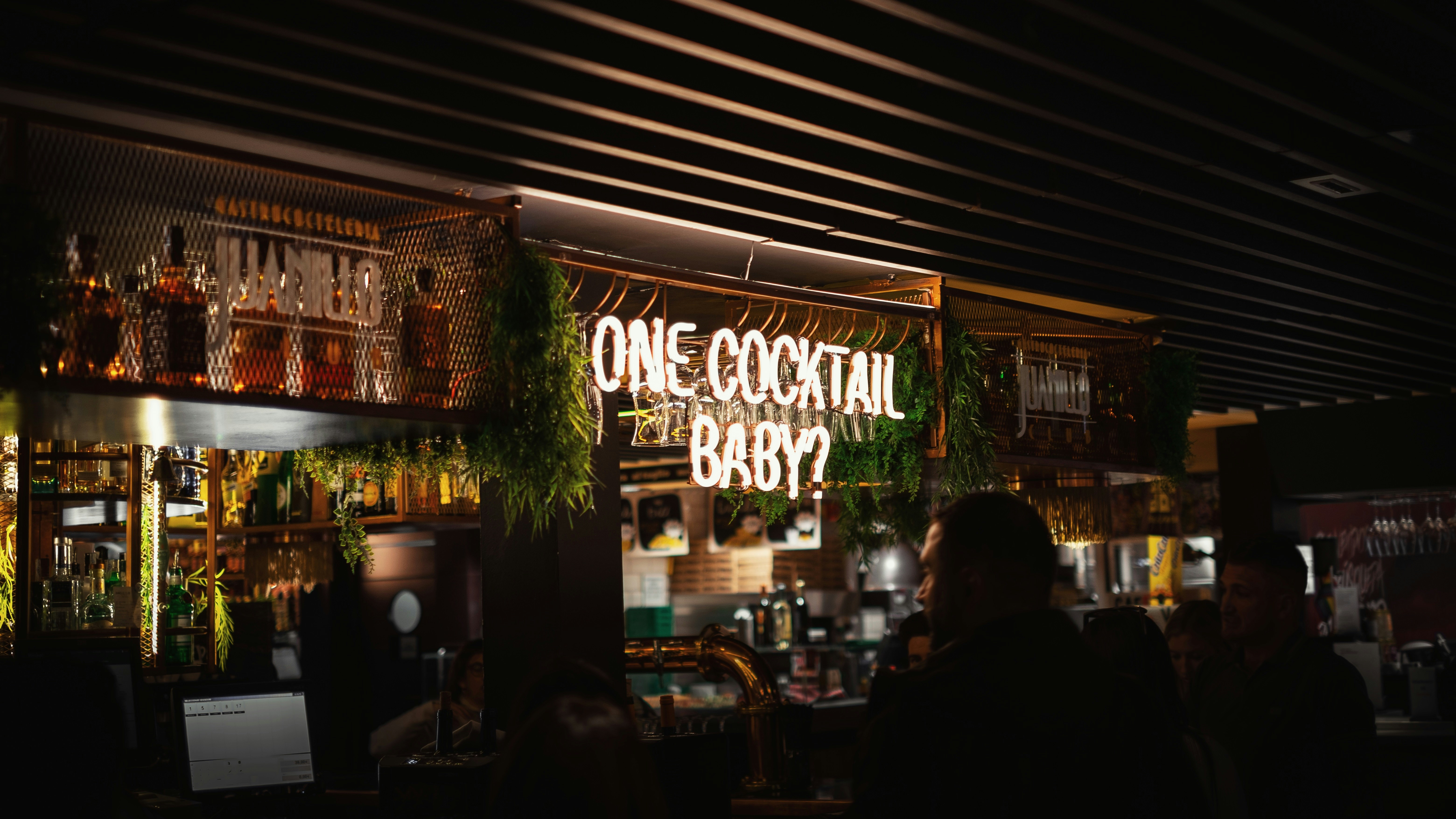 man in black shirt standing in front of brown wooden table, Neon "one cocktail baby?"