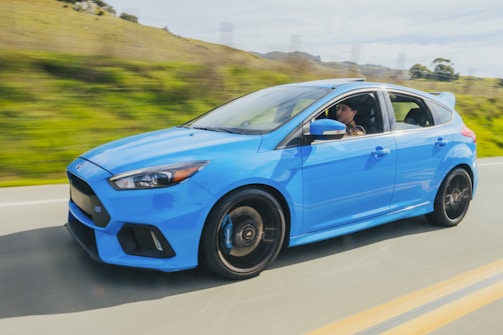 A shiny blue sports car speeding along a coastal highway