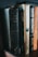 Several books stand side-by-side on a wooden shelf. The titles visible include religious and fiction genres, with one book titled 'The Living Bible' having a notably worn black cover. Other books have spines with dark, beige, and orange tones, and are authored by popular writers.