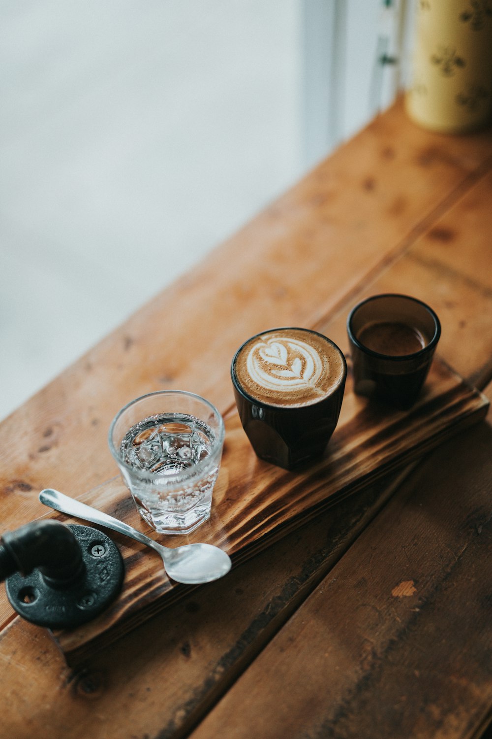 clear drinking glass beside silver spoon and black ceramic mug on brown wooden table