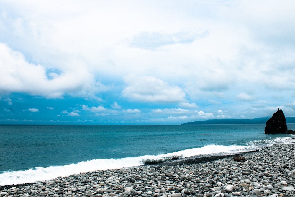 ocean waves crashing on shore under white clouds and blue sky during daytime