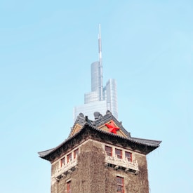 A traditional Chinese-style building is topped with a large red star and covered with ivy. Behind it, a modern skyscraper with a sleek design towers against a clear blue sky.