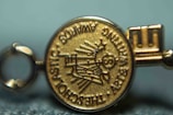 A close-up view of a gold medallion with embossed text and symbols. The text appears around the edge of the medallion and includes words like 'SCHOLASTIC' and 'AWARDS'. The central design features a depiction of a globe and stylized sun rays.