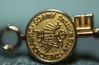 A close-up view of a gold medallion with embossed text and symbols. The text appears around the edge of the medallion and includes words like 'SCHOLASTIC' and 'AWARDS'. The central design features a depiction of a globe and stylized sun rays.