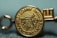 A close-up view of a gold medallion with embossed text and symbols. The text appears around the edge of the medallion and includes words like 'SCHOLASTIC' and 'AWARDS'. The central design features a depiction of a globe and stylized sun rays.