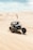 A dune buggy is racing across expansive sand dunes under a partly cloudy sky. A small flag on the vehicle flutters in the breeze, while the sand is kicked up by the spinning wheels.