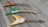 Three electric guitars are laid out on a wooden deck. Each guitar has a distinct color: one red with a flame design, one green with white accents, and one yellow with cream accents. They are arranged in a diagonal line, creating a visually appealing composition.
