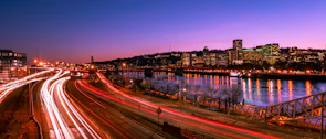A vibrant cityscape at dusk with glowing lights reflecting on the river.