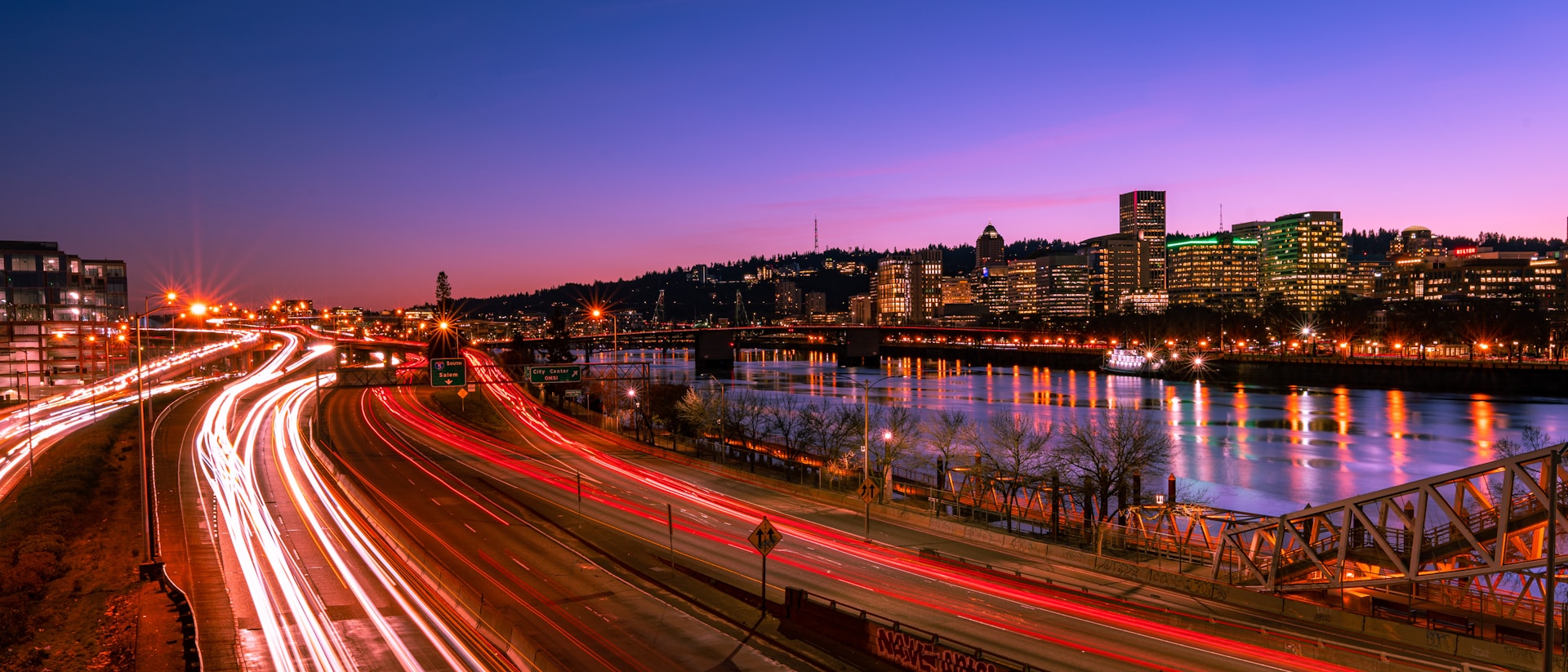 A vibrant cityscape at dusk, with glowing lights reflecting on a calm river.