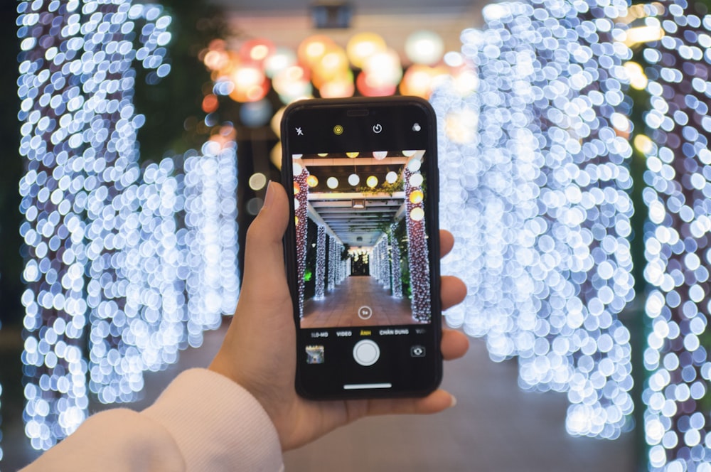 person holding iphone taking photo of white and blue lighted christmas tree