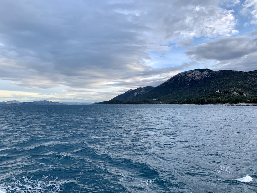 body of water near mountain under cloudy sky during daytime