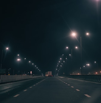 A tow truck lifting a car on a quiet highway at dusk with flashing lights.