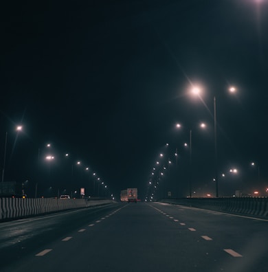 Nighttime shot of a freight truck illuminated by streetlights on an empty road.