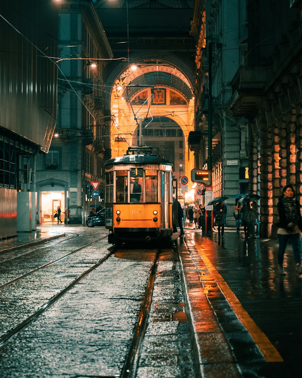 Persone che camminano sul marciapiede vicino al tram giallo durante la notte