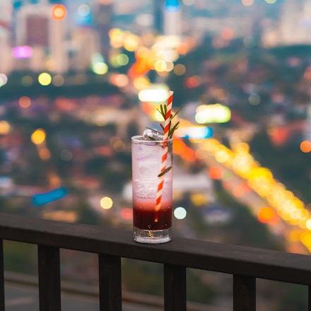 A vibrant cocktail being poured into a glass with a city skyline blurred in the background.