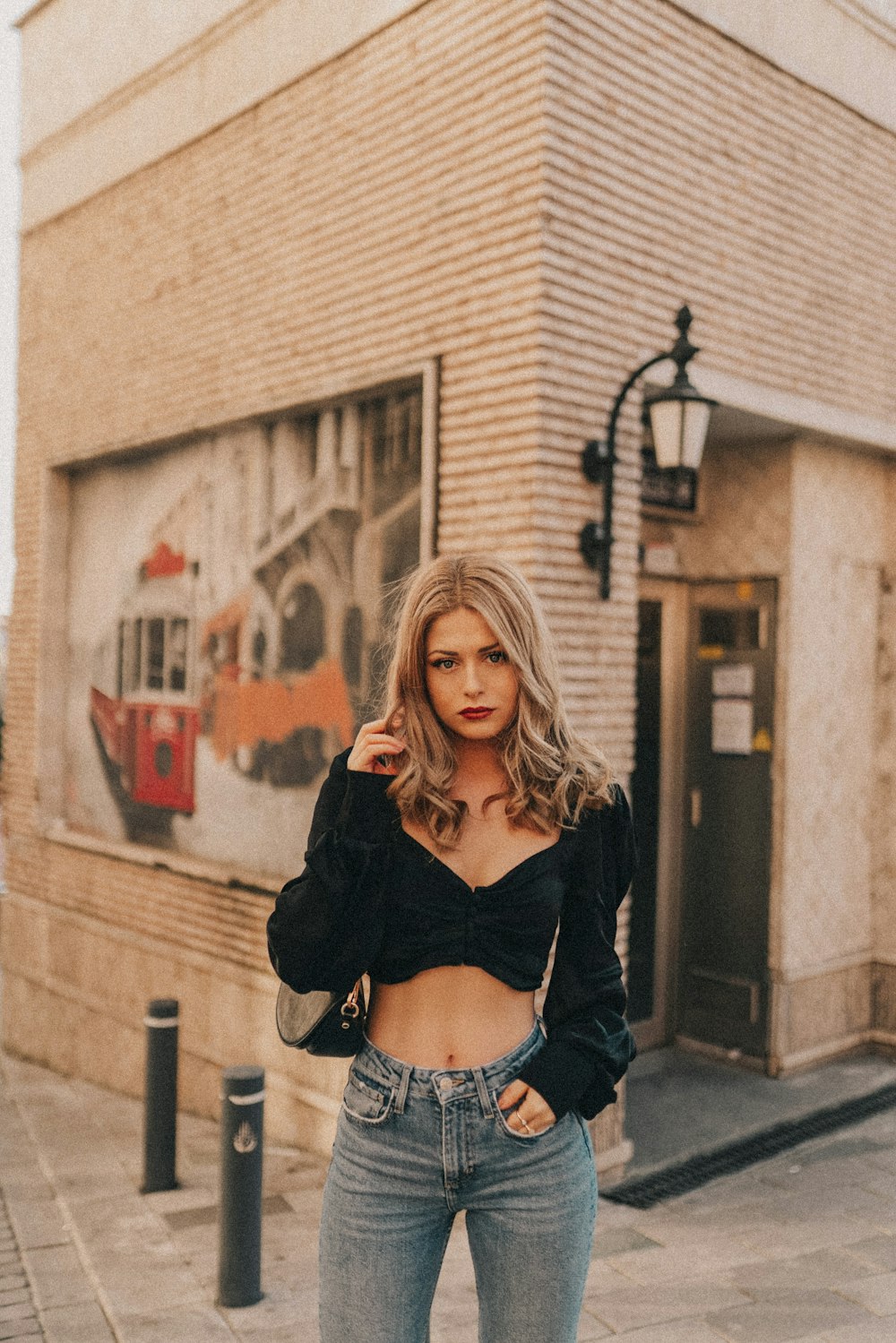 woman in black cardigan and white crop top standing near brown brick building during daytime