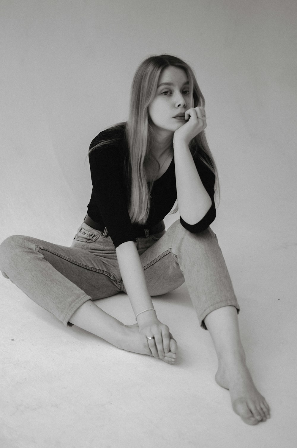 Femme en chemise à manches longues noire et jean en denim gris assise sur un sol blanc