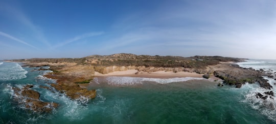 brown and green mountain beside body of water during daytime in Porto Covo Portugal