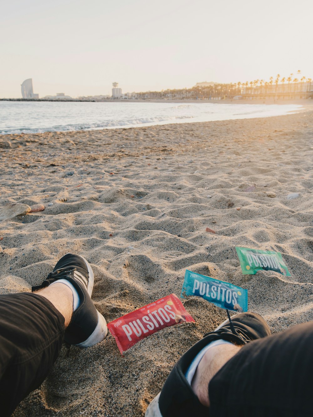 person in brown shorts and black and white sneakers sitting on beach sand during daytime