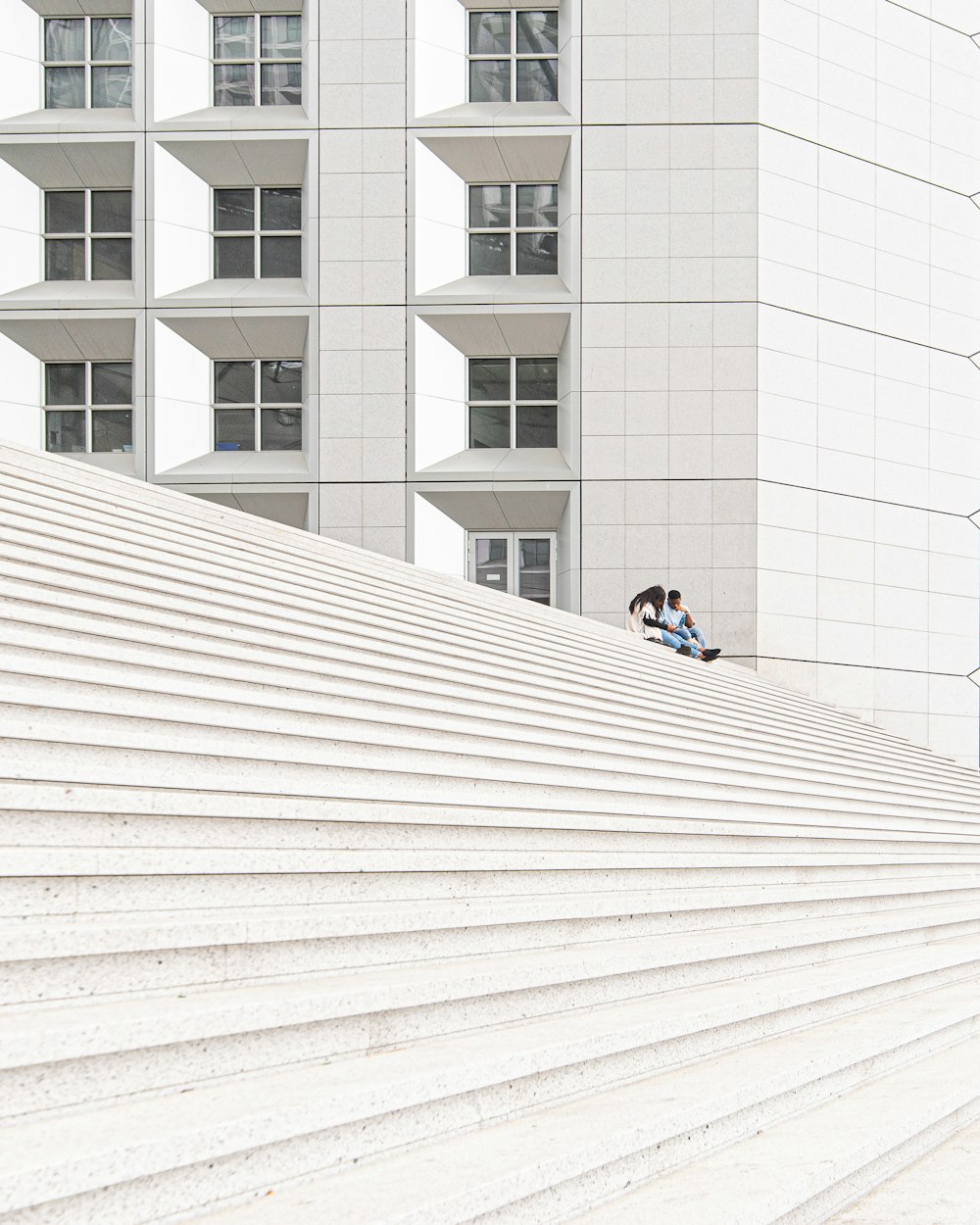 uomo in giacca nera che si siede sul pavimento di cemento bianco durante il giorno