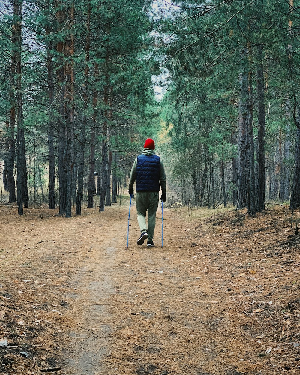 uomo in giacca nera e pantaloni neri che cammina sulla strada sterrata marrone nella foresta durante il giorno