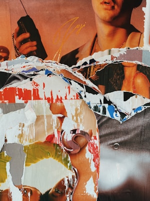 A collage composed of torn paper layers revealing fragments of images including a person holding an object resembling a walkie-talkie, colorful designs, and parts of human figures. The torn edges create a chaotic, textured appearance.