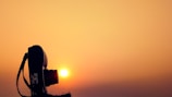 High contrast image of a film camera silhouette against a bright horizon over the ocean.